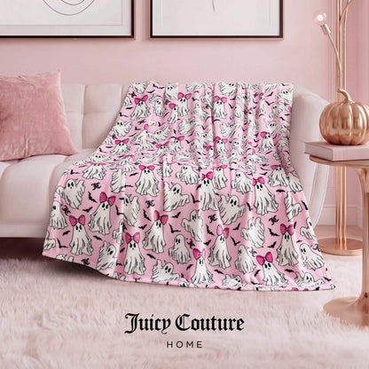 The Halloween Plush Throw Blanket 50" x 60", featuring white cartoon ghost dogs with pink bows, is draped over a sofa in a chic pink-themed living room—an adorable Juicy Couture Home accent for Halloween decor.
