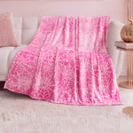 The Halloween Plush Throw Blanket 50" x 60" in pink with a white web pattern is draped over a white couch in a pastel-themed room with a plush white rug, pink pillow, and copper lamp—adding cozy Halloween décor.