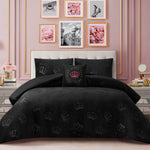 A bedroom with a pink accent wall, floral decor, and framed art. The bed features a tufted headboard adorned with the Embossed Plush Crown Comforter Set, which showcases elegant crown patterns and includes a matching decorative pillow.