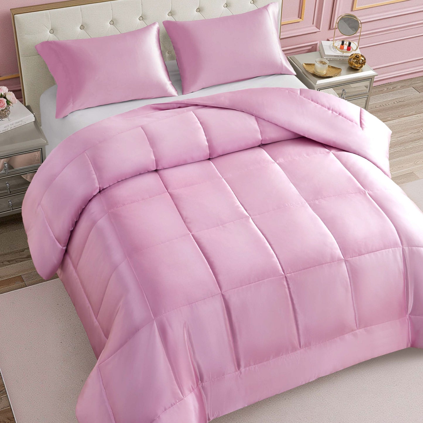 A neatly made bed features the Solid Satin Down Alternative Comforter in light pink, providing all-season warmth and paired with matching pillows; the room showcases elegant decor, including a tufted headboard, nightstands, and soft pink walls.