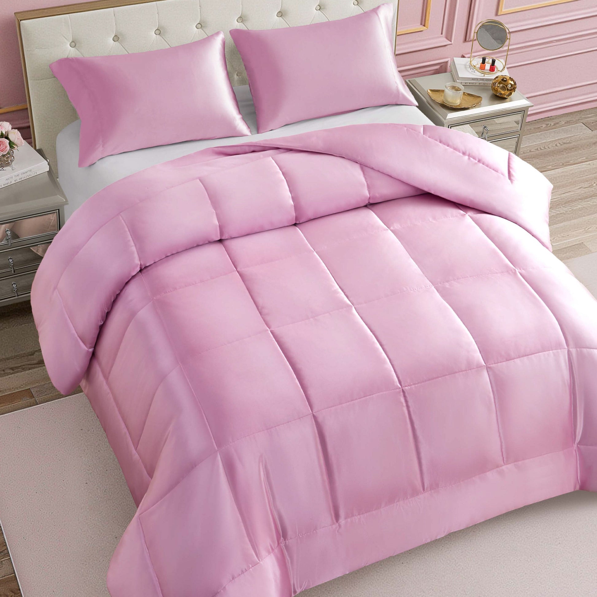 A neatly made bed features the Solid Satin Down Alternative Comforter in light pink, providing all-season warmth and paired with matching pillows; the room showcases elegant decor, including a tufted headboard, nightstands, and soft pink walls.