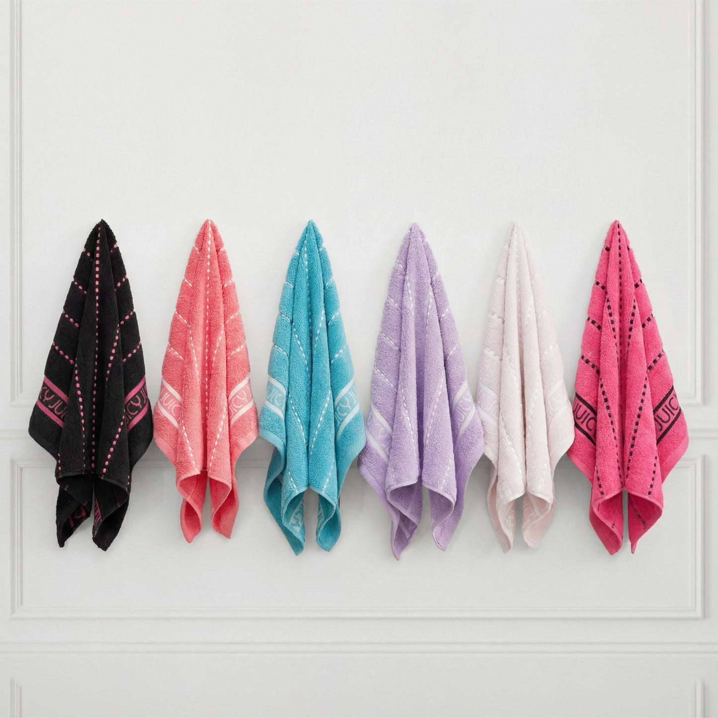 The Plush Stripe Bath Towel Set includes six ultra-soft towels in black, coral, turquoise, purple, white, and pink with small patterns and decorative borders, neatly displayed on white hooks against a white wall.