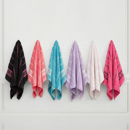 The Plush Stripe Bath Towel Set includes six ultra-soft towels in black, coral, turquoise, purple, white, and pink with small patterns and decorative borders, neatly displayed on white hooks against a white wall.