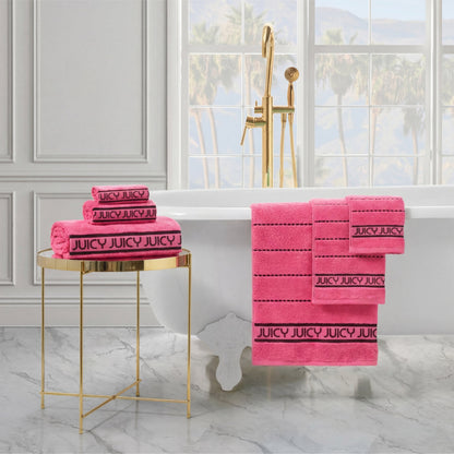 Plush Stripe Bath Towel Set in bright pink is neatly folded and hanging in a luxurious bathroom featuring a white clawfoot tub, gold fixtures, a round gold side table, and a window with palm trees outside.