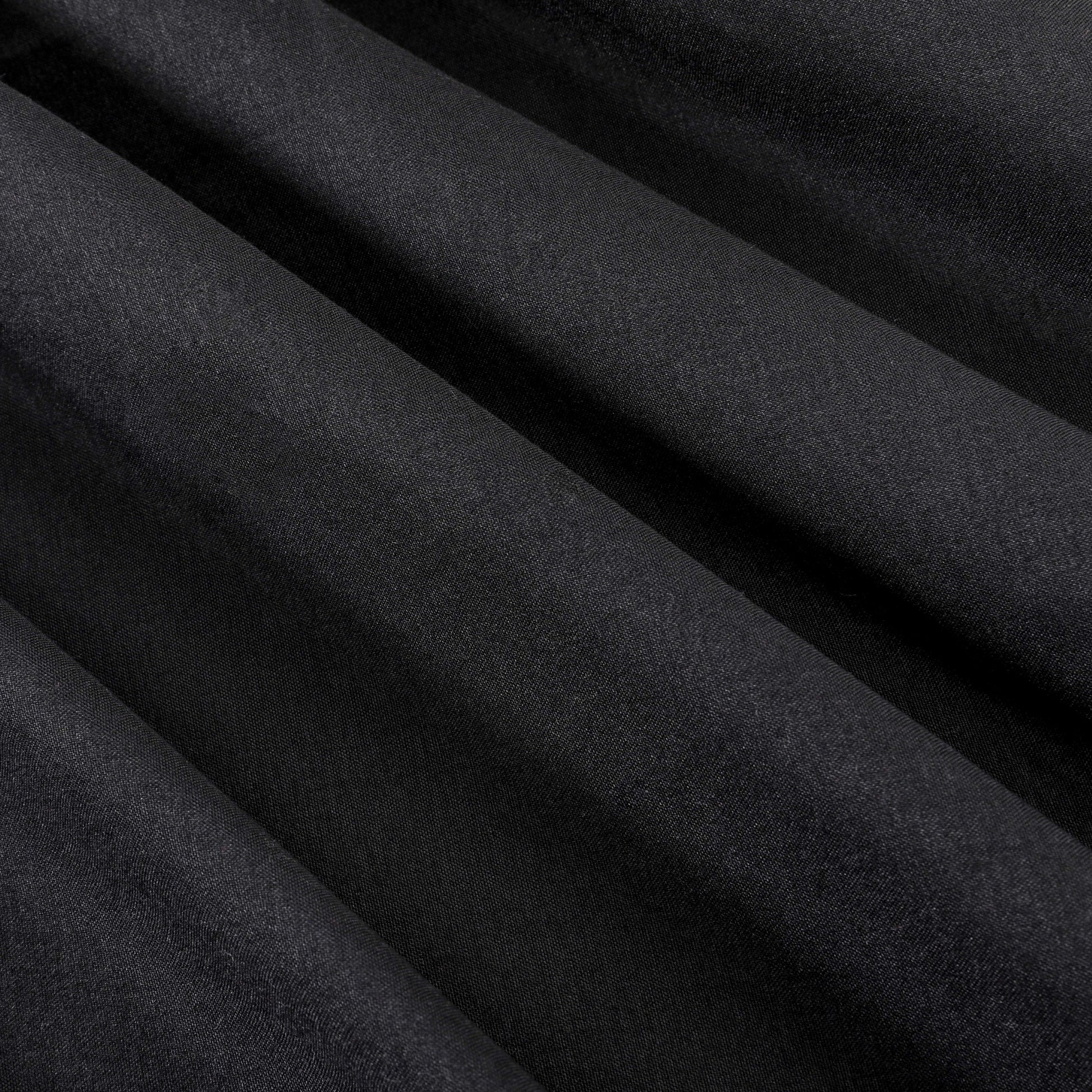 Close-up of smooth, black fabric with diagonal folds creating soft shadows and highlights across the surface, evoking the elegance of a luxury bedding collection such as the Microfiber Sheet Set With Extra Pillowcases.