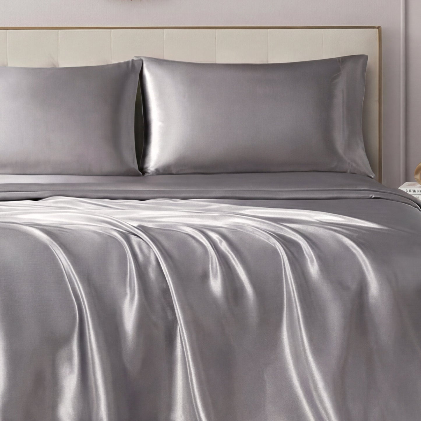 A neatly made bed showcases the Solid Satin Sheet Set with ultra-soft sheets and pillowcases, paired with a light-colored upholstered headboard for a luxurious, elegant look.