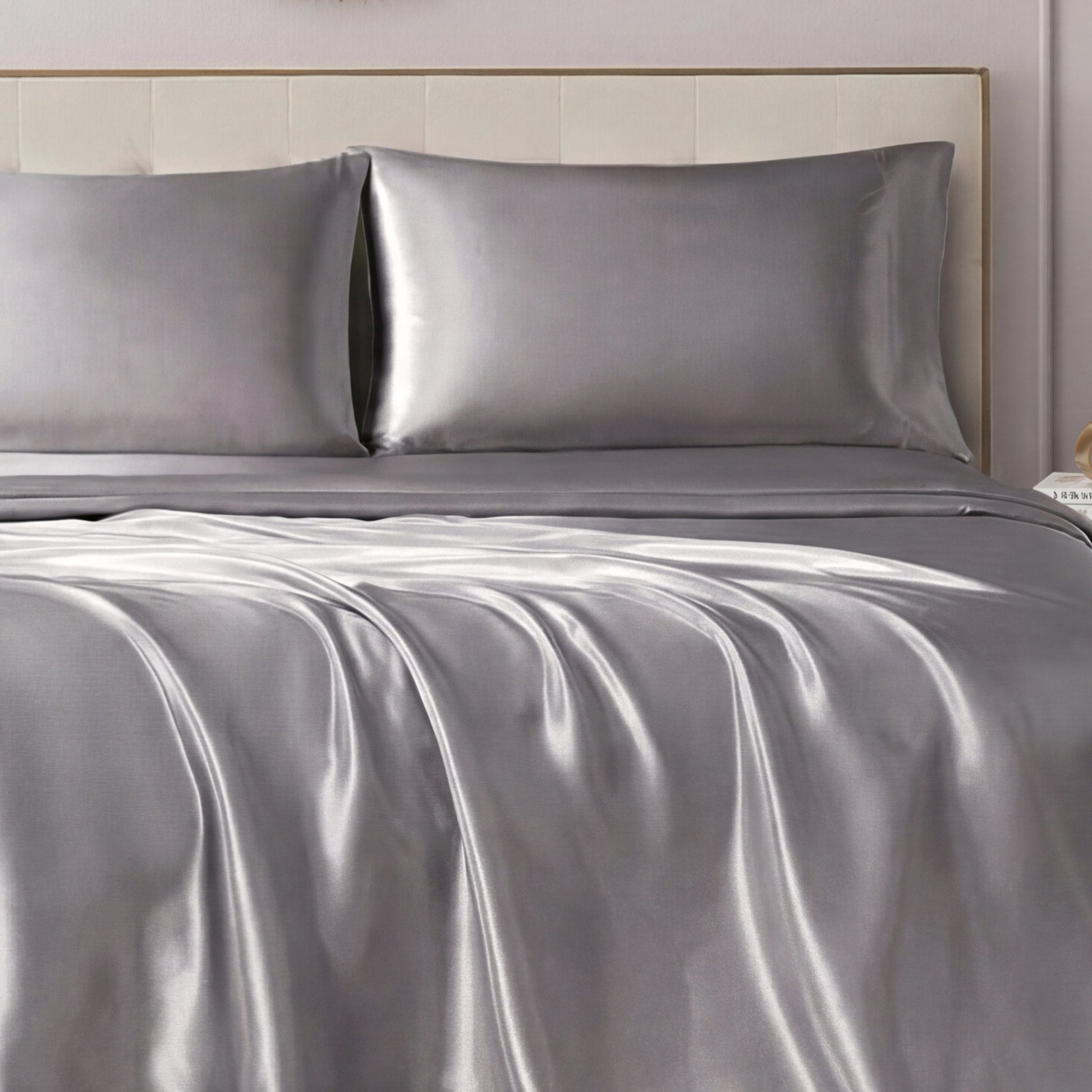 A neatly made bed showcases the Solid Satin Sheet Set with ultra-soft sheets and pillowcases, paired with a light-colored upholstered headboard for a luxurious, elegant look.