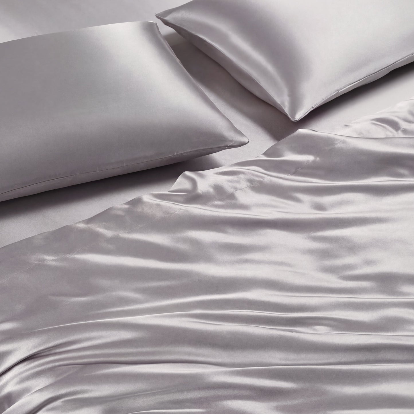 Two silver-gray pillows and the Solid Satin Sheet Set are neatly arranged on a bed, creating a smooth, shiny surface with gentle folds and a luxurious look.