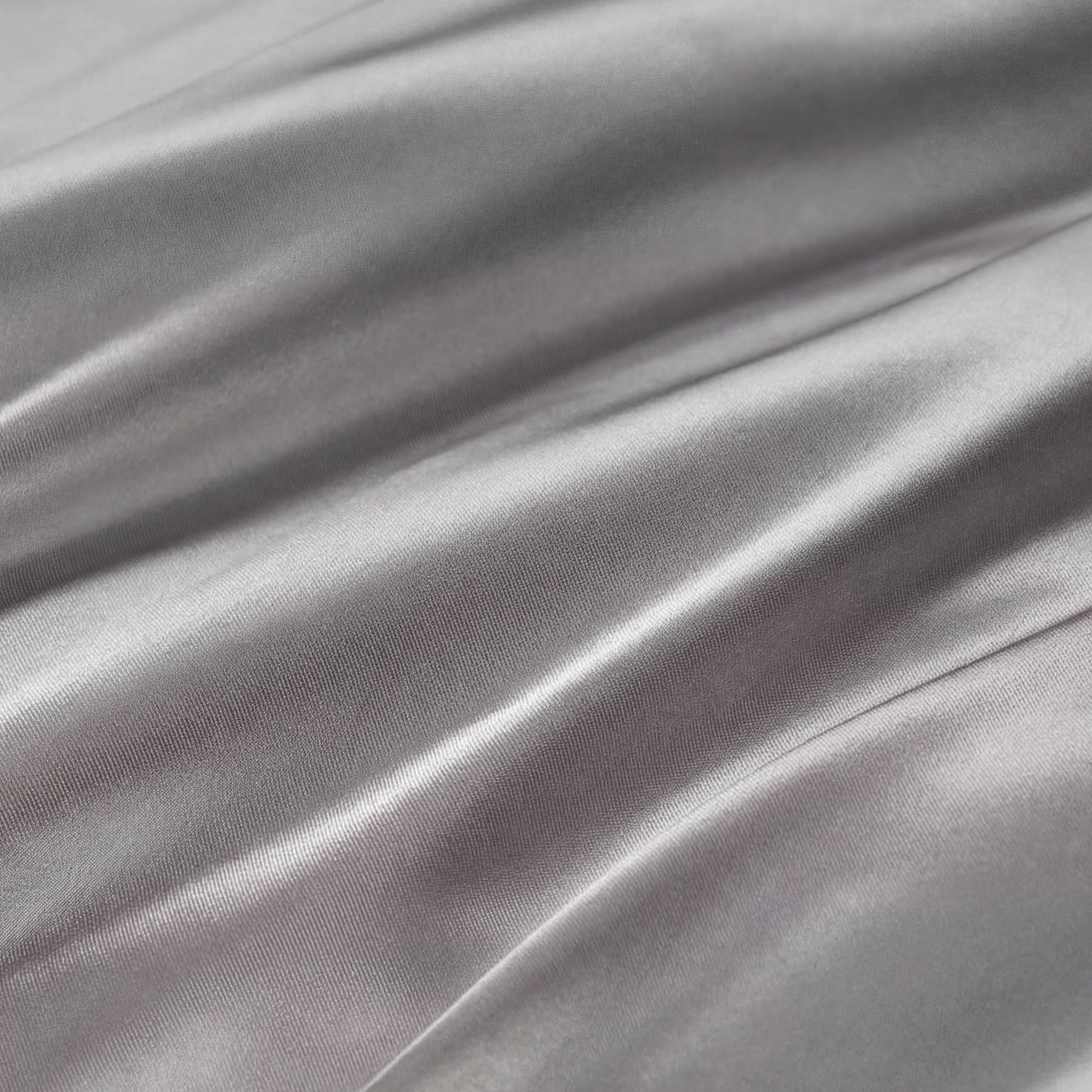 Smooth, shiny silver-gray fabric with gentle folds and soft reflections highlights the silky texture of the Solid Satin Sheet Set—perfect for adding a touch of ultra-soft luxury to your bedroom.