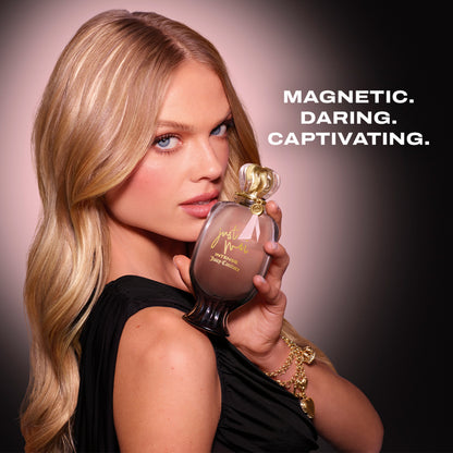A woman with long blonde hair holds a Just Moi Intense Eau de Parfum Spray Pen, 0.33 oz, near her face. She wears a black dress and gold bracelet. Bold text on the right reads: “MAGNETIC. DARING. CAPTIVATING.”.