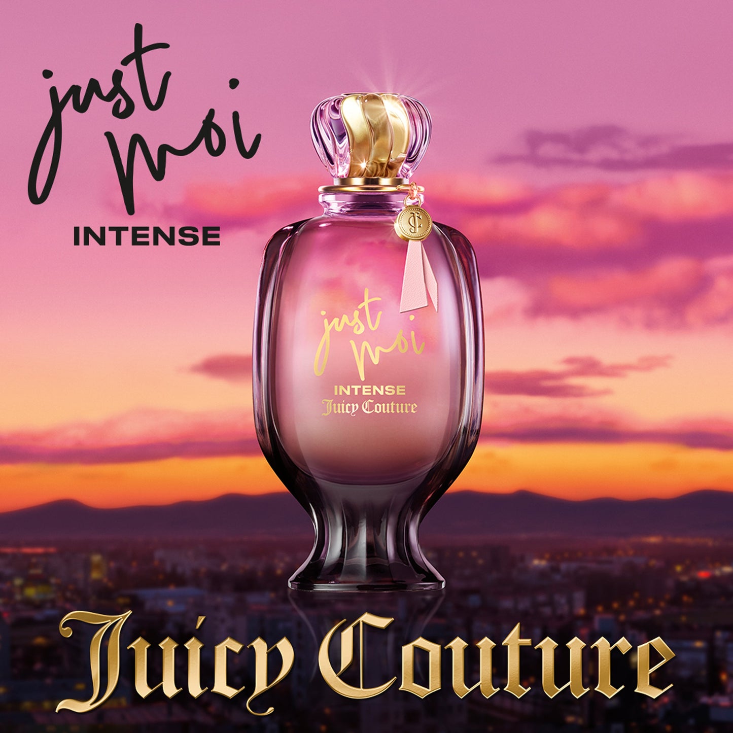 A pink and gold Just Moi Intense Eau de Parfum Spray Pen, 0.33 oz, an Amber Vanilla scent by Juicy Couture, stands before a sunset cityscape with pink and purple skies. "Juicy Couture" appears in gold at the bottom.