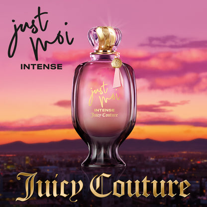 A pink and gold Just Moi Intense Eau de Parfum Spray Pen, 0.33 oz, an Amber Vanilla scent by Juicy Couture, stands before a sunset cityscape with pink and purple skies. "Juicy Couture" appears in gold at the bottom.