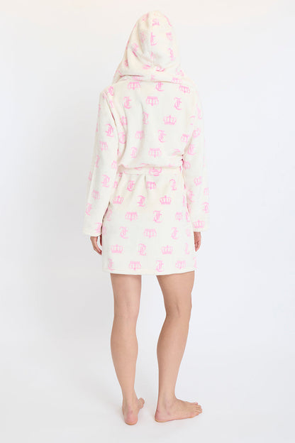 A person stands barefoot facing away, wrapped in the Hooded Luxe Plush Robe featuring pink crowns and letters, against a plain white background.