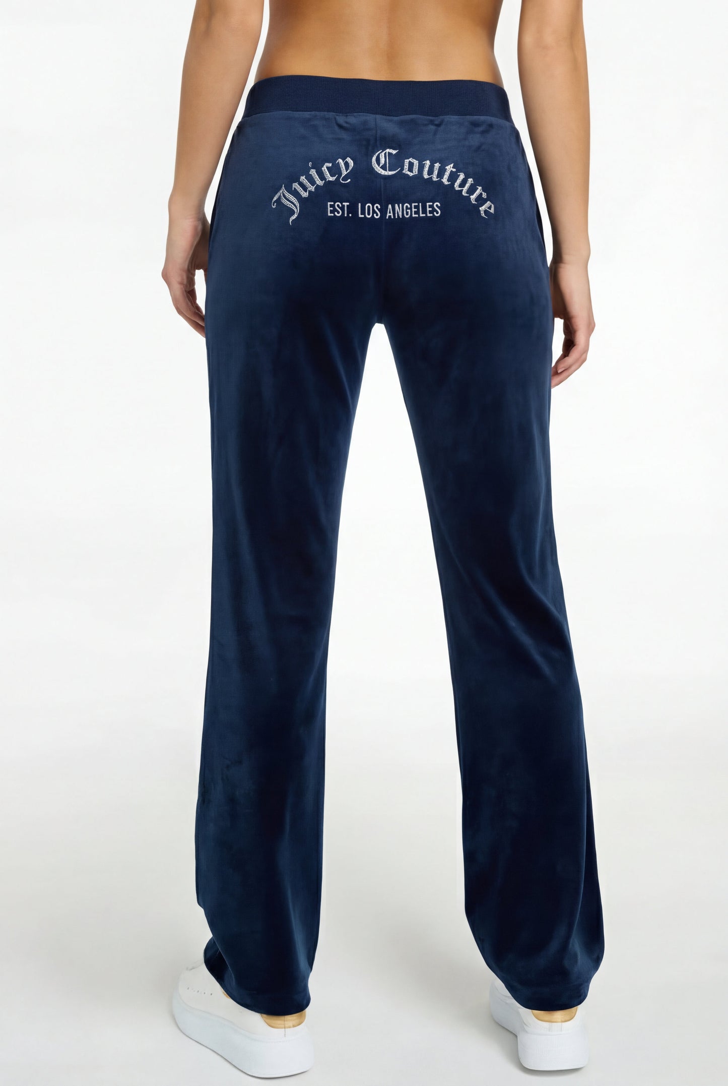 A woman is shown from the back wearing a Crochet Maxi Dress with a colorful hem, paired with navy velour pants featuring "Juicy Couture EST. LOS ANGELES" in white text on the back and white sneakers.