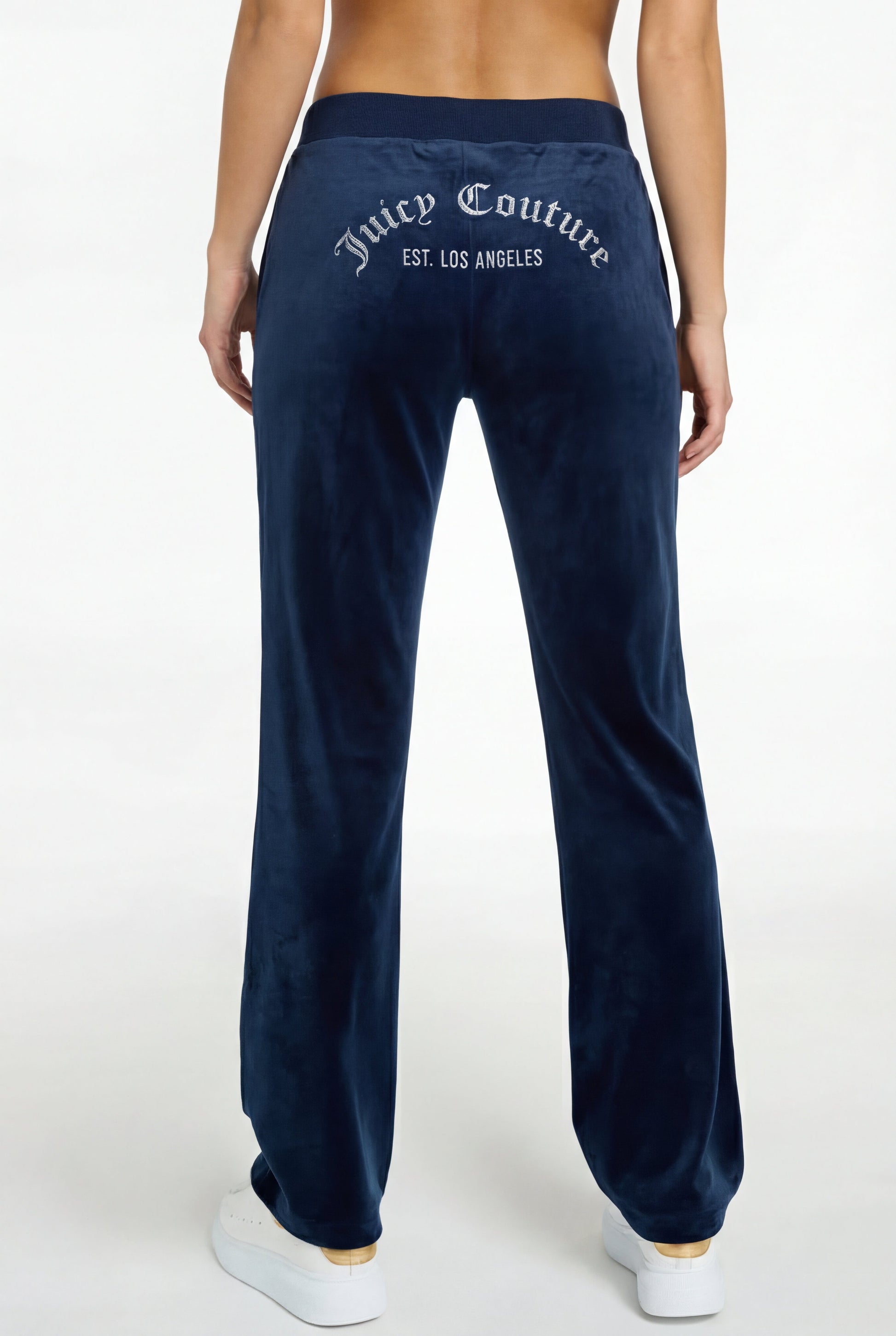 A woman is shown from the back wearing a Crochet Maxi Dress with a colorful hem, paired with navy velour pants featuring "Juicy Couture EST. LOS ANGELES" in white text on the back and white sneakers.