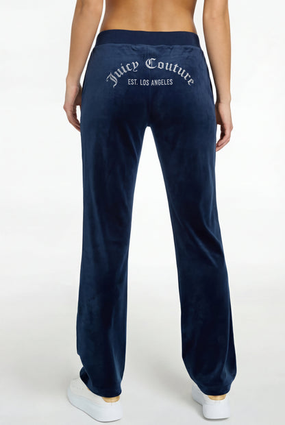A woman is shown from the back wearing a Crochet Maxi Dress with a colorful hem, paired with navy velour pants featuring "Juicy Couture EST. LOS ANGELES" in white text on the back and white sneakers.